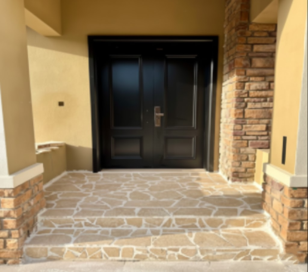Residential front entryway with natural limestone paver flooring, black double door, and stacked stone accent columns.png